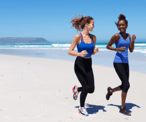 wellness supplements: Two girl friends jogging on the beach smiling at one another