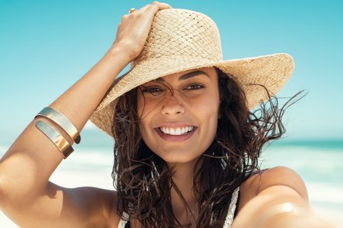 Beautiful woman on the beach in summer smiling with a wide brimmed hat on her head